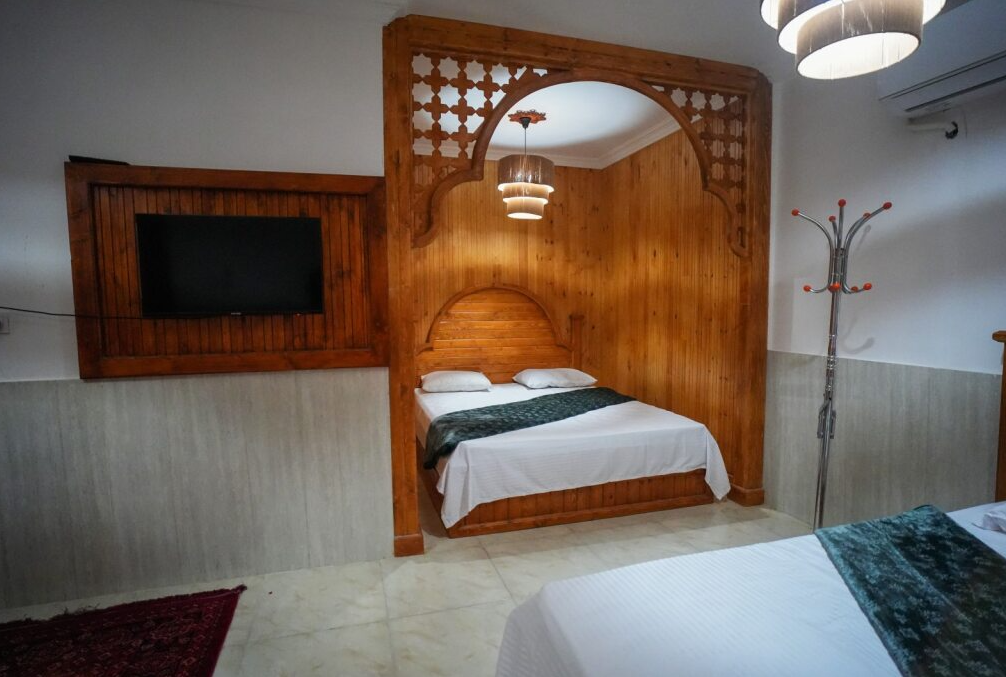 اتاق‌خواب با تخت دونفره و دیوارکوب چوبی در بوم‌گردی میرزا قشم