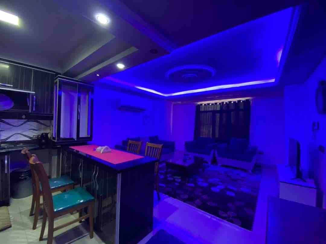نشیمن با نورپردازی LED بنفش و مبلمان فیروزه‌ای در آپارتمان سام پلاس قشم