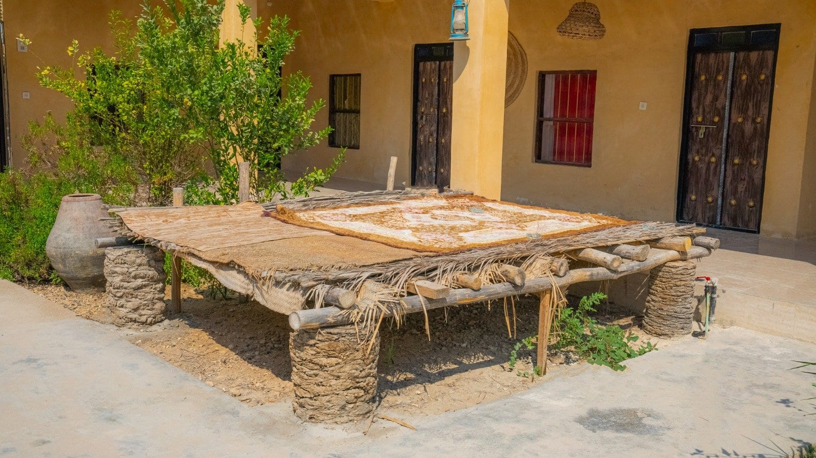 میزِ چوبیِ بزرگ روی سکوی نشیمنِ بیرونی در حیاطِ بوم‌گردی میرزا قشم