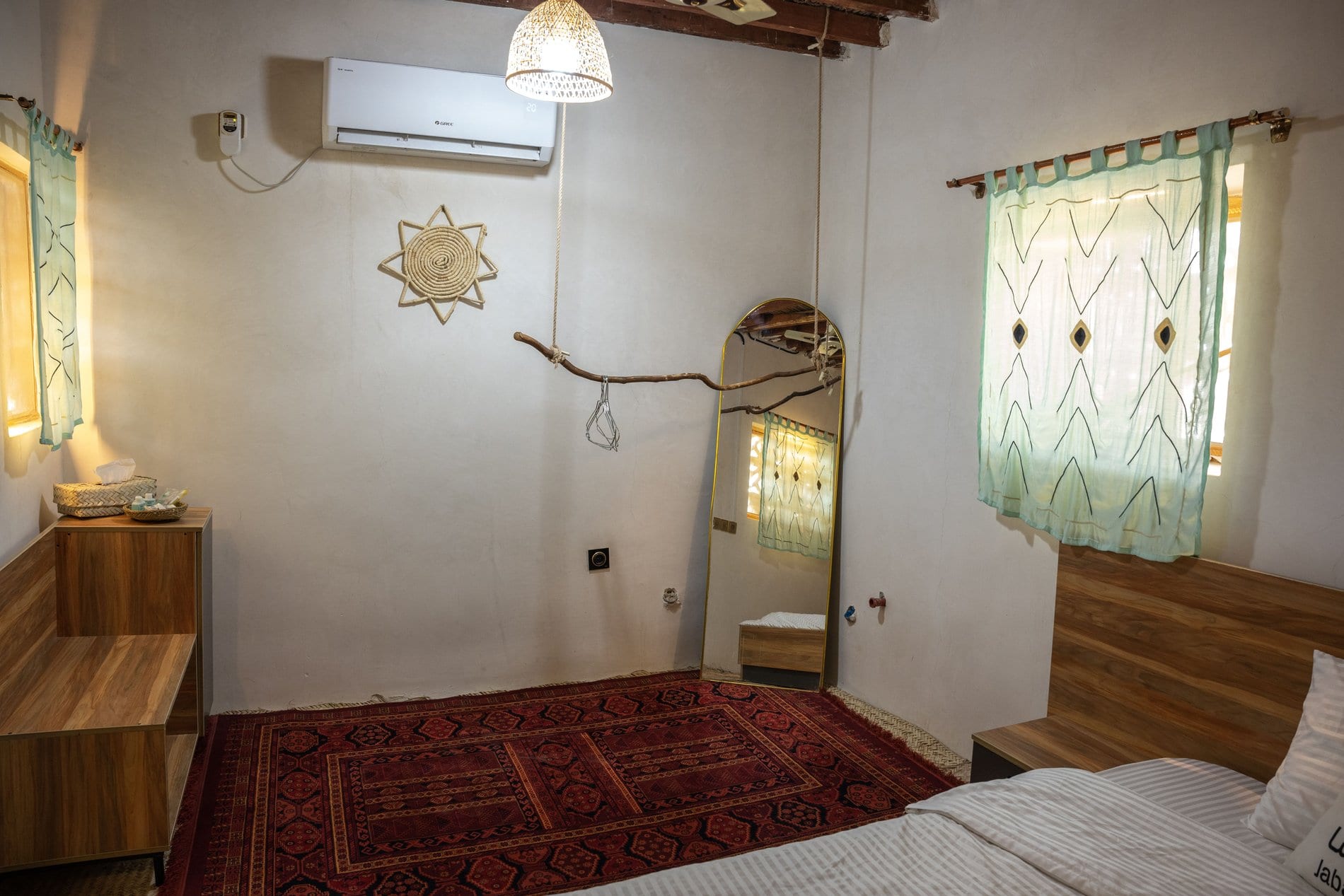 اتاق‌خواب با کولر، کنسول چوبی، آینهٔ قدی و فرش دستباف سرخ در بوم‌گردی خانه مانگرو قشم