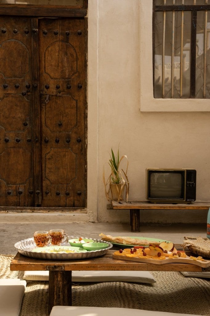 میزِ پذیراییِ کوتاه با چایِ سنتی و میوه روبه‌روی تلویزیونِ قدیمی در خانه مانگرو قشم