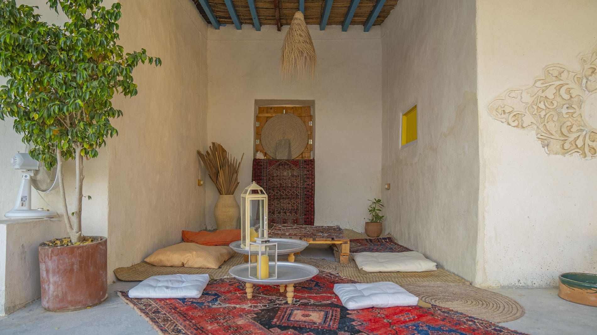 اتاق پذیرایی سنتی با کوسن، فرش و دیوار کاهگلی در بوم‌گردی نهان قشم