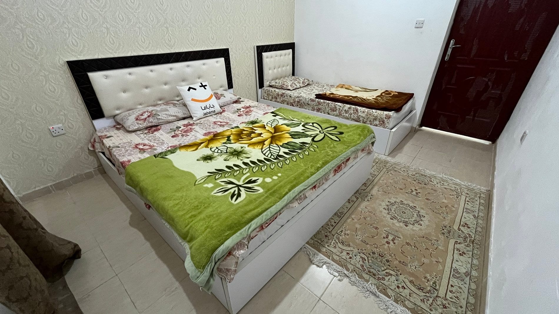 اتاق‌خواب با تخت دونفره و روتختی گل‌دار سبز در واحد مبله مجتمع قشم