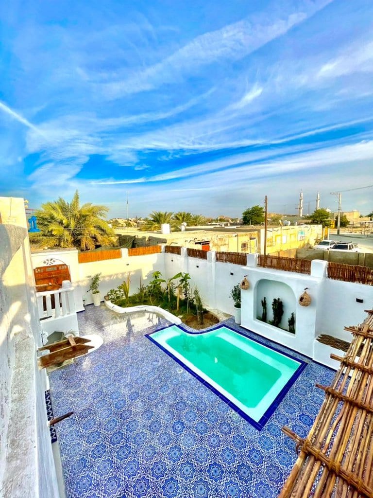 استخر و نمای بیرونی بنای سفید قوسی زیر آسمان آبی در اقامتگاه بوم‌گردی خانه ماهی قشم