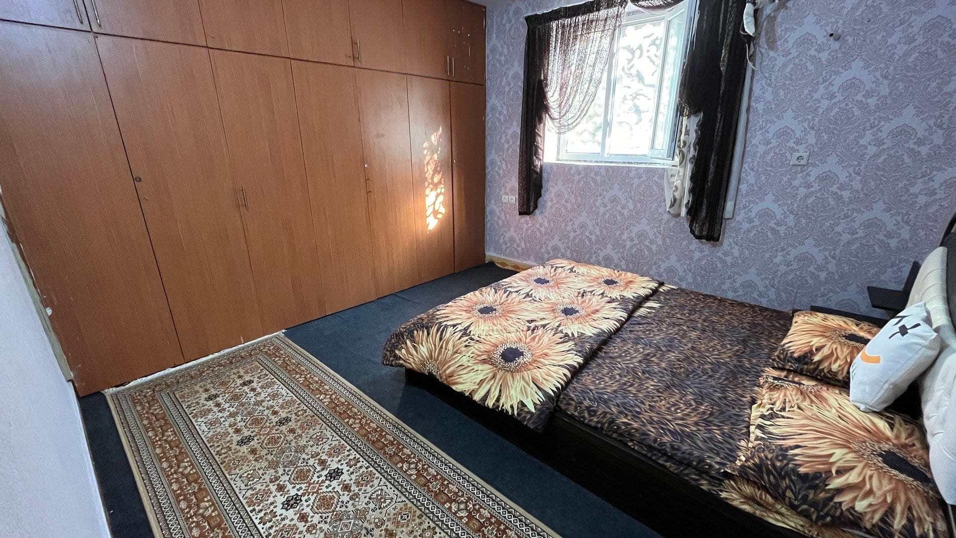 اتاق‌خواب با تخت، روتختی گل‌دار و پنجره در آپارتمان ۶۰متری قشم