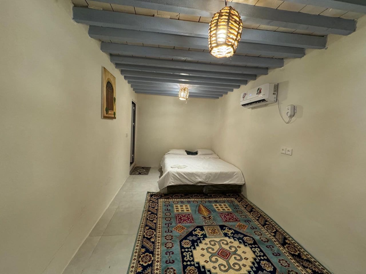 اتاق‌خواب واحد با تخت دونفره، کولر و فرش دستباف در بوم‌گردی گل ابریشم قشم