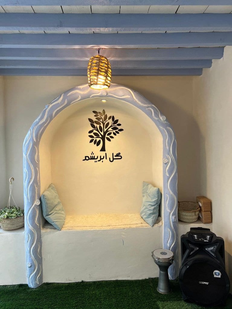 طاقچهٔ نشیمن گنبدی با کوسن و لوگوی «گل ابریشم» روی دیوار در بوم‌گردی گل ابریشم قشم