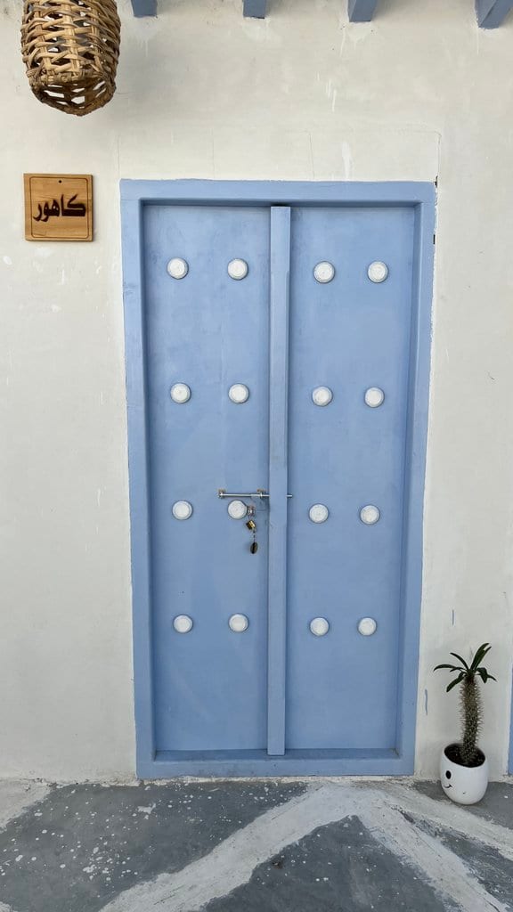 در آبی واحد کهور با تابلوی نام و معماری سفید در بوم‌گردی گل ابریشم قشم