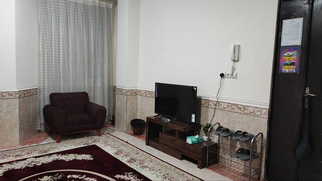 پذیرایی مبله با مبل راحتی و فرش قرمز در آپارتمان دوخوابه قشم