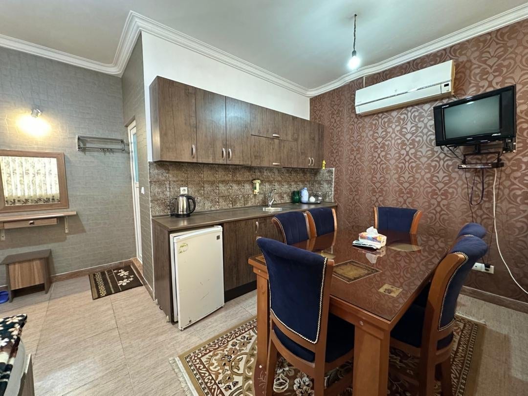 آشپزخانهٔ کوچک با کابینت، یخچال و چای‌ساز و میز نهارخوری در واحد پونه قشم