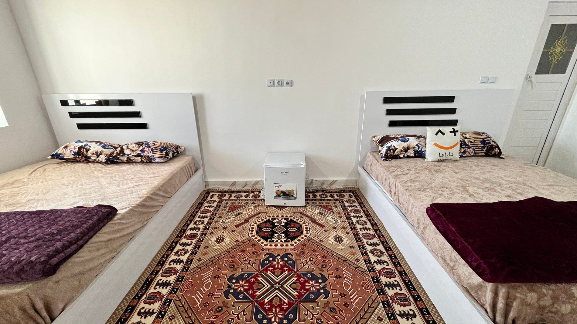 اتاق با رخت‌خواب سنتی روی فرش و تابلوی دیواری در بوم‌گردی لاور قشم