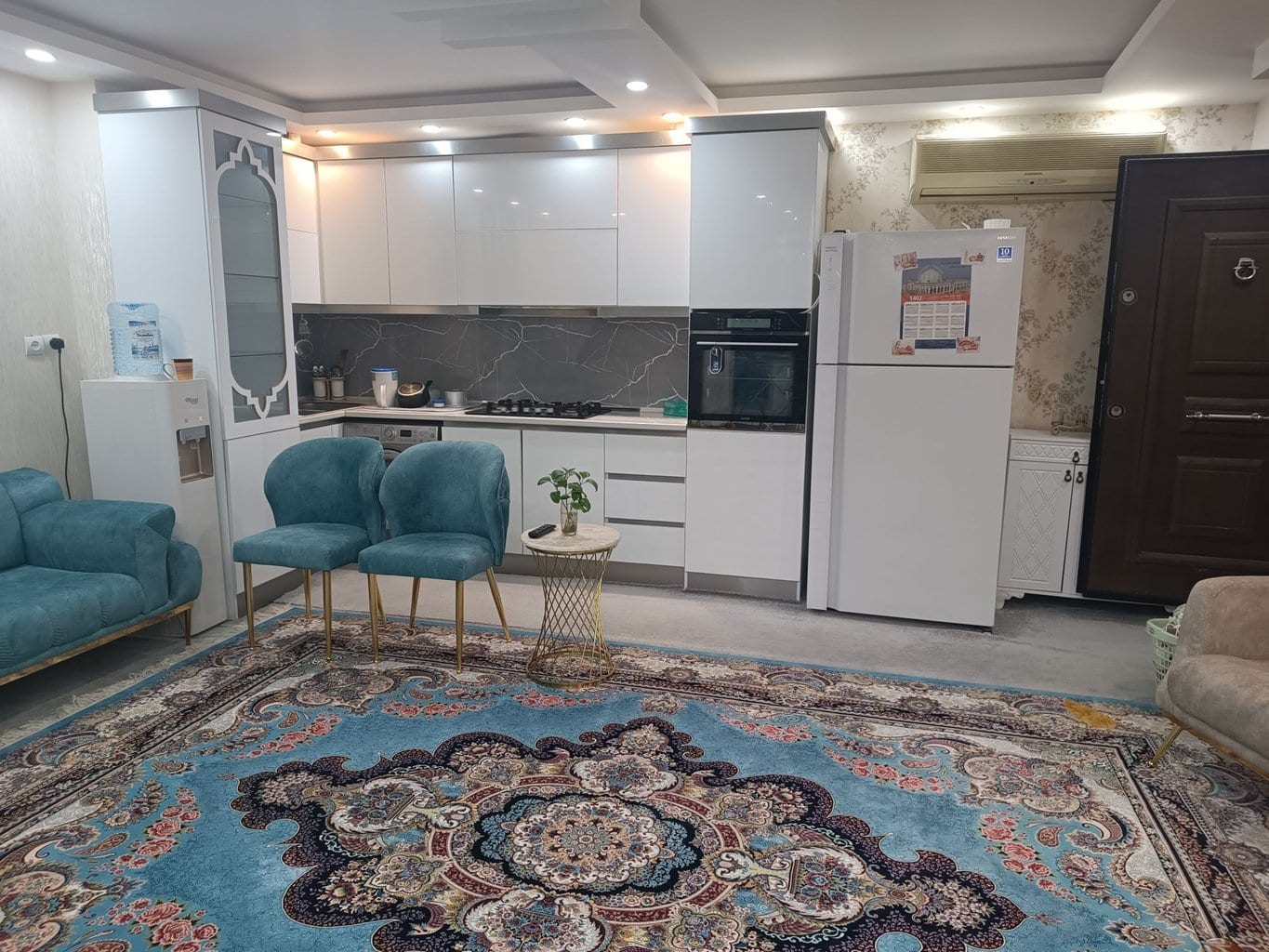 آشپزخانهٔ کامل با کابینت سفید و یخچال در آپارتمان فیروزه‌ای قشم