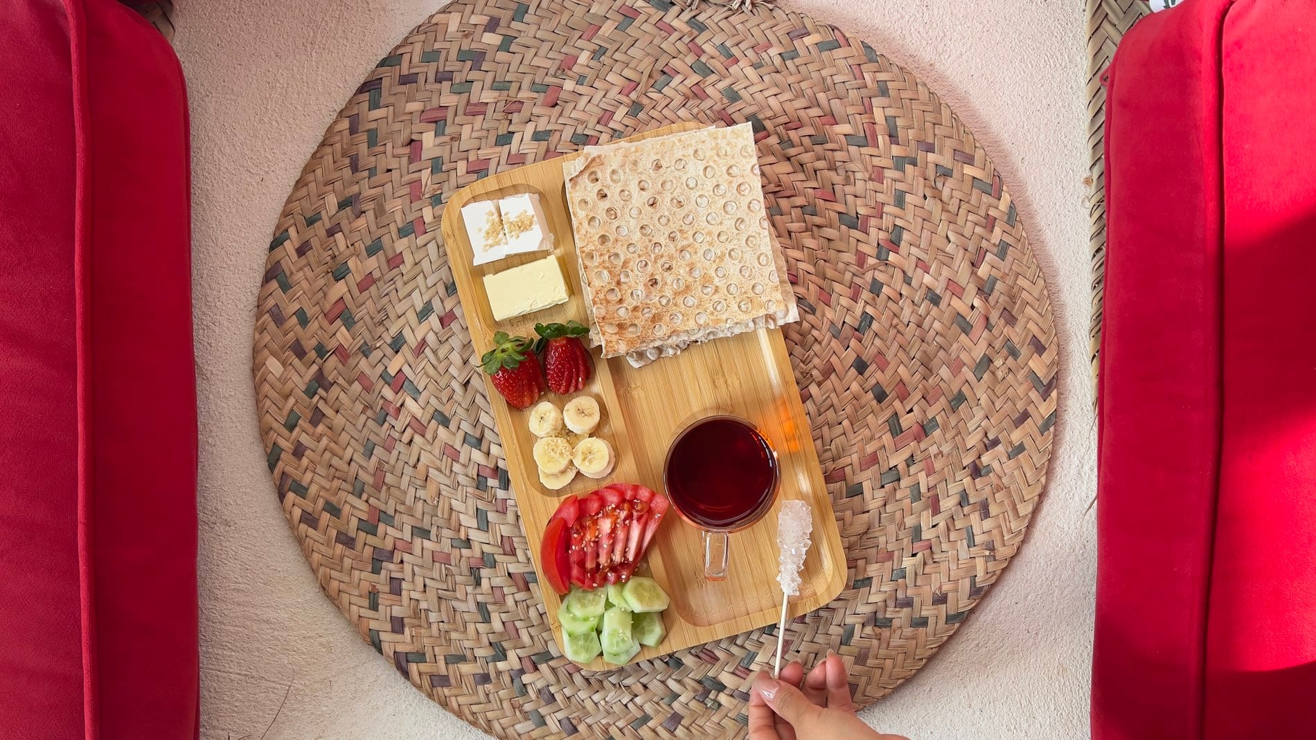 صبحانهٔ سنتی چیده‌شده روی فرشِ حصیری میان پشتی‌های قرمز در بوم‌گردی خانه کوچ هرمز