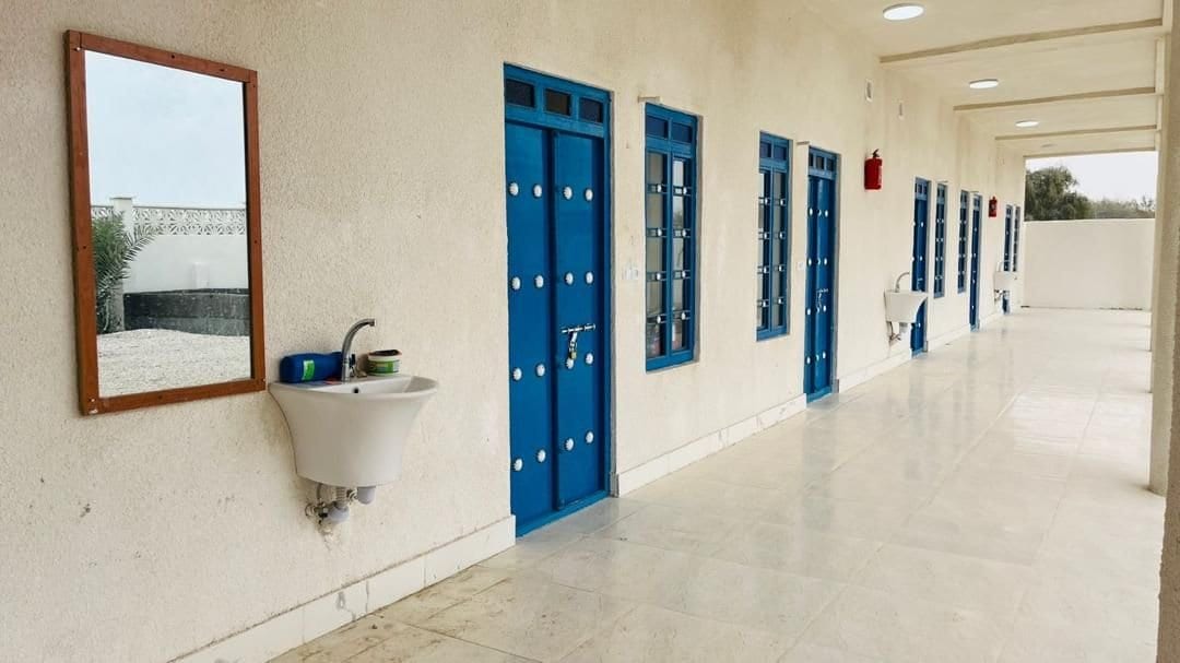 راهروی واحدها با درهای آبی، آینه و روشوییِ دیواریِ بیرونی در بوم‌گردی ناخدا عبدالصالح قشم
