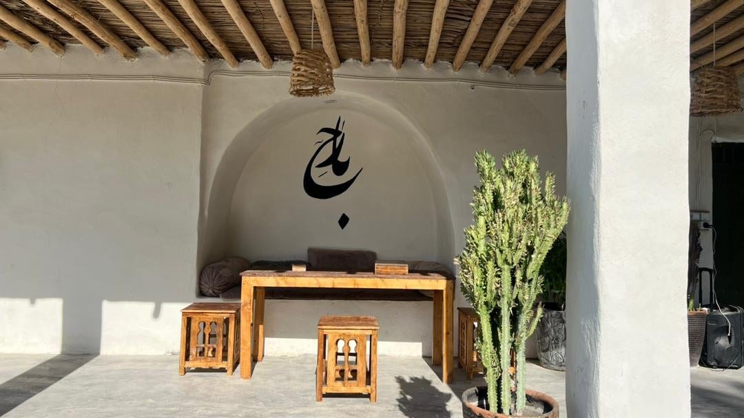 نشیمن سنتی با میز چوبی و تابلوی خطاطی در بوم‌گردی بارح قشم