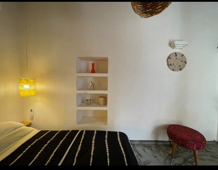 گوشهٔ اتاق‌خواب با طاقچهٔ دیواری، چراغ زرد و چهارپایهٔ قرمز در بوم‌گردی خانه باور