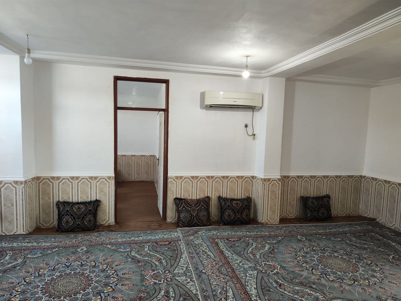 نشیمنِ سنتی فرش‌شده با پشتی و راهرو به اتاق‌خواب در سوئیت سنتی سه‌نفره قشم
