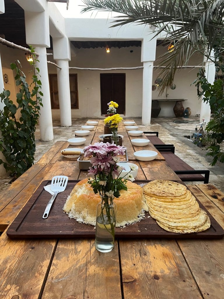میز غذای دسته‌جمعی با نان محلی و گل در حیاط بوم‌گردی دورشه قشم